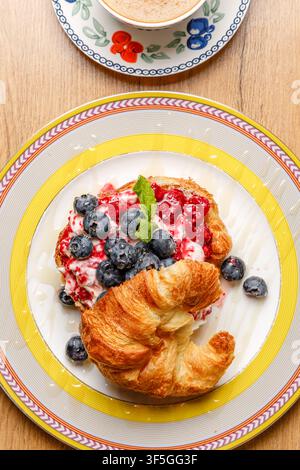 Sandwich croissant alla moda con formaggio burrata, bacche fresche e caffè Foto Stock