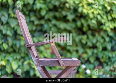 Vista laterale di una sedia da giardino in legno stagionato contro una vegetazione verde rigogliosa con messa a fuoco selettiva Foto Stock