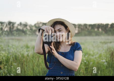 Fotografa sorridente che rivede le foto sulla fotocamera in un prato estivo Foto Stock