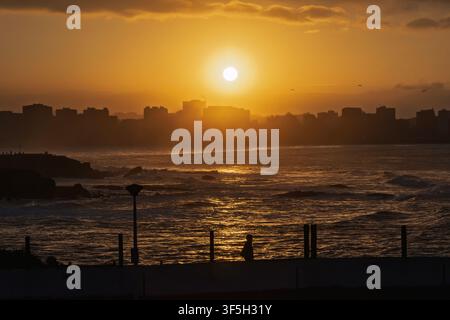 Tramonto sulla città di Gijon con la silhouette di un passante e la città sullo sfondo. Asturie, Spagna Foto Stock
