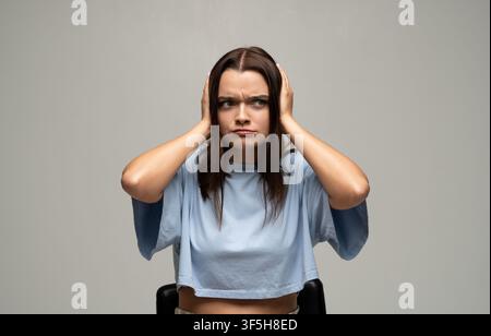 Giovane donna che si copre le orecchie, si sente stressata e frustrata dal rumore forte, subisce un sovraccarico sensoriale Foto Stock