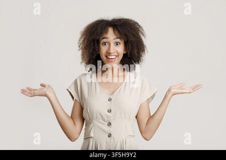 Scioccata ed eccitata donna millenaria afroamericana con occhi aperti stendendo le braccia ai lati Foto Stock