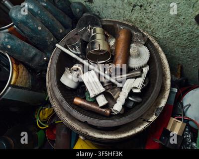 Varie parti metalliche vecchie, ingranaggi, molle, bulloni e tubi in una ciotola arrugginita in officina. Rottami industriali e pezzi di ricambio. Concetto di disordine nel garage di riparazione. Foto Stock