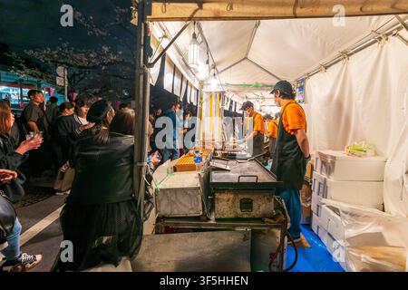 Persone in fila per acquistare snack caldi da un vivace chiosco di cibo in un mercato notturno a Nakameguro durante il festival dei fiori di ciliegio primaverili. Foto Stock