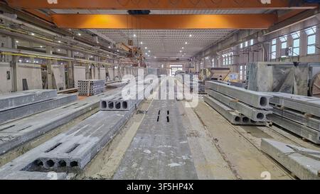 Laboratorio di fabbrica industriale che produce lastre e travi in calcestruzzo prefabbricato a nucleo cavo con una gru sospesa. Foto Stock