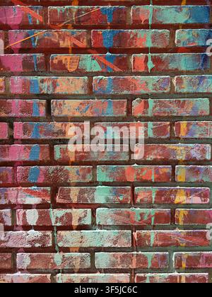 Primo piano di un muro di mattoni invecchiato coperto da vernice graffiti multicolore sbiadita, superfici scheggiate, malta ruvida e texture urbana invecchiata per un'atmosfera vibrante Foto Stock