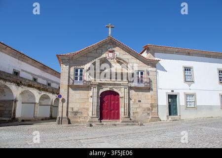 Antico edificio ecclesiastico con una porta rossa e una facciata in pietra su una strada acciottolata Foto Stock