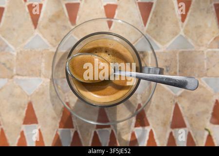 Vista dall'alto di un espresso appena preparato servito in una tazza di vetro trasparente su un tavolo decorativo a mosaico marocchino. Crema di caffè ricca Foto Stock