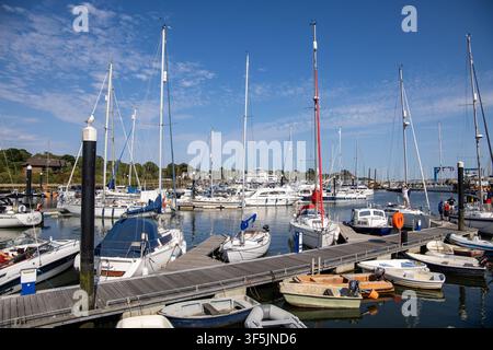 Molte barche a vela e motoscafi ormeggiati in una marina con moli di legno in una giornata di sole splendente con cielo azzurro a Lymington, Hampshire, Regno Unito Foto Stock
