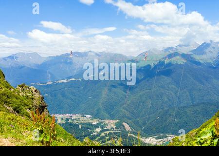 Un piano grandangolare di una persona che attraversa un ponte sospeso ad alta quota fatto di cavi e assi, sospeso tra le vette montuose. La scena Foto Stock