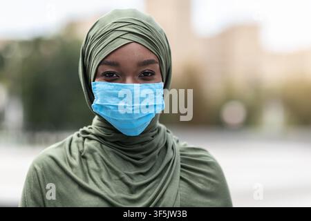 Donna musulmana africana felice in hijab indossando maschera facciale protettiva all'aperto Foto Stock