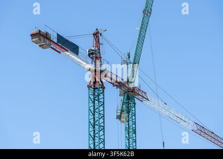 Vista a basso angolo di gru torre e getti di calcestruzzo sospesi in un cantiere, con telai in acciaio, cavi e macchinari silouettati contro un Foto Stock