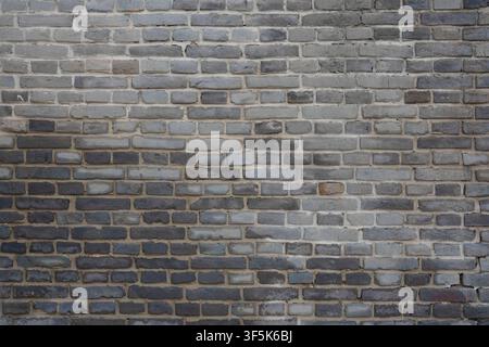 Questa texture ad alta risoluzione mostra un muro di mattoni grigio invecchiato con superfici ruvide e irregolari e malta di cemento consumata visibile tra ogni blocco. La Foto Stock