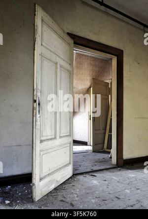 Porte aperte all'interno di una stazione ferroviaria abbandonata, creando profondità e atmosfera in un edificio storico trascurato. Foto Stock