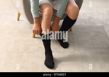Uomo che indossa calzini di compressione neri mentre è seduto su una sedia, concetto di salute e benessere, supporto medico per le gambe Foto Stock