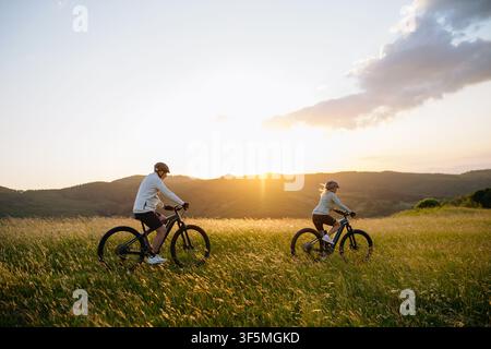 Coppia di anziani in bicicletta nella natura, che guardano il tramonto. Foto Stock