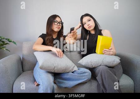 Due donne indonesiane che si godono una serata cinema con popcorn guardando la televisione insieme in un ambiente domestico confortevole. Foto Stock