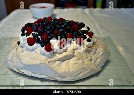 Torta pavlova alla meringa ricoperta di panna montata, mirtilli e lamponi su piatto di vetro Foto Stock