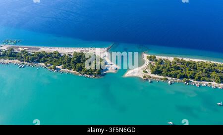 Acque turchesi di una laguna circondano una stretta spiaggia sabbiosa e una penisola ricoperta di alberi con piccole barche ormeggiate lungo la costa in Grecia. Foto Stock