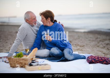 Una coppia di anziani innamorati per un romantico picnic sulla spiaggia in riva al mare. Foto Stock