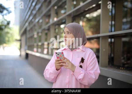Giovane donna musulmana con telefono in strada cittadina Foto Stock
