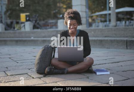 Donna nera felice che lavora sul suo laptop all'aperto Foto Stock