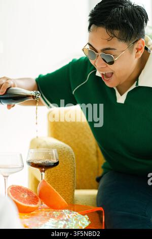 Persona elegante con occhiali da sole che versa con entusiasmo una bevanda Foto Stock