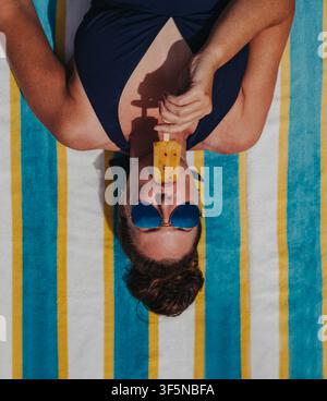 Donna che assapora un ghiacciolo su un asciugamano a righe visto dall'alto Foto Stock