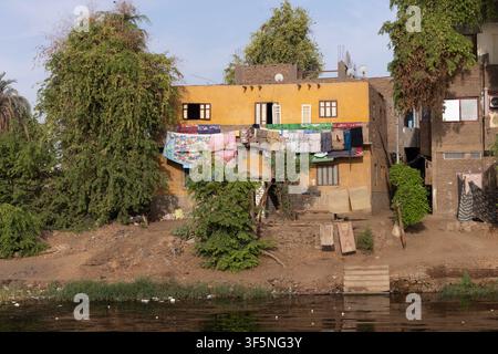 Il bucato colorato si asciuga lungo il balcone del primo piano su una facciata ocra intonacata a calce di una casa rurale in mattoni di fango lungo il fiume Nilo in Egitto. Foto Stock