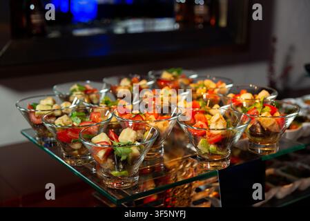 Più ciotole di vetro trasparente sono disposte su un tavolo da buffet, ognuna ripiena di un'insalata vivace con verdure tritate, crostini ed erbe. L'ind Foto Stock
