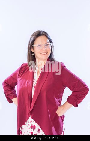 Sarah Gray è in piedi in un'area luminosa con un sorriso amichevole. Indossa una giacca rossa sopra un top a fiori e ha gli occhiali. Le sue mani sono sui fianchi mentre Foto Stock