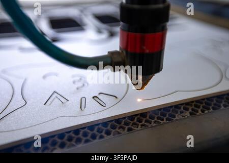 Macchina laser CNC industriale che incide forme intricate su una superficie di foglio di plastica bianca utilizzando un fascio di luce ad alta intensità focalizzato da una misurazione automatizzata Foto Stock