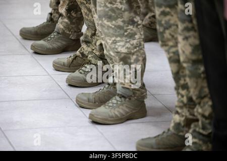 Soldati delle forze armate ucraine che indossano uniformi moderne a mimetismo digitale e stivali tattici stanno in fila professionale su pavimento piastrellato, mostrando Foto Stock