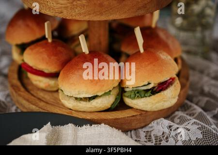 Mini burger slider disposti su un vassoio di servizio in legno a due livelli, ideali per il catering per feste, eventi o presentazioni di pasti rustici, antipasti Foto Stock