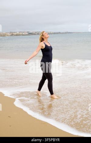 Donna che si sente libera e si connette con la natura camminando tra le onde dell'oceano Foto Stock