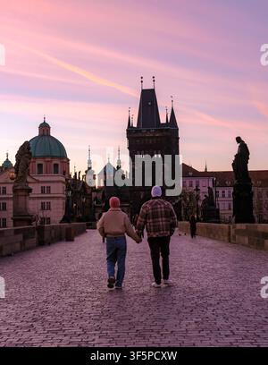 Una coppia si tiene per mano mentre attraversa il ponte Carlo storico a Praga mentre un tramonto mozzafiato tinge il cielo. Foto Stock