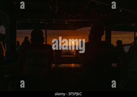 Persone che osservano il tramonto da un bar sulla spiaggia in silhouette sulla Big Island delle Hawaii Foto Stock