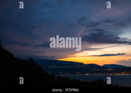 Alba mattutina sulle colline del Lago di Garda, Italia, con luci tremolanti lungo la baia Foto Stock