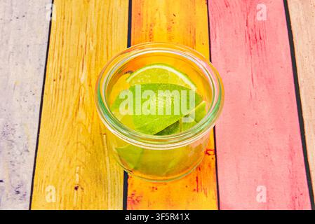 Spiedini di lime freschi che si immergono in un barattolo di vetro su un tavolo di legno dipinto a colori vivaci Foto Stock