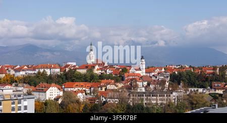 Dron filma la città di Kranj in Slovenia con tetti rossi, chiesa e montagne sullo sfondo durante il giorno. Foto Stock
