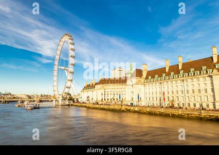 Vista della ruota panoramica del London Eye sulle rive del Tamigi con l'edificio storico del County Hall sotto un cielo blu terso a Londra, Inghilterra Foto Stock