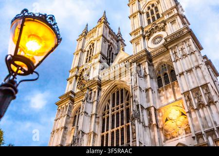 Vista della facciata gotica ornata e delle torri dell'Abbazia di Westminster illuminata da un lampione vicino contro un cielo blu a Londra, Inghilterra, Regno Unito Foto Stock