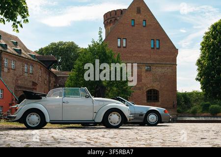 Berlino, Germania – 3 maggio 2026. Vista laterale di una Volkswagen Beetle cabriolet bianca parcheggiata accanto a una roadster Mercedes argentata nel cortile della Zitadella Foto Stock