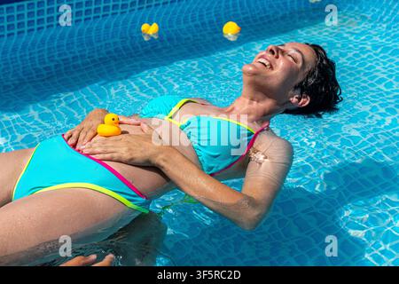 Donna incinta che galleggia in una piscina con un papera di gomma Foto Stock