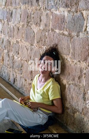 Donna che sorride e scrive in un diario mentre ascolta musica Foto Stock