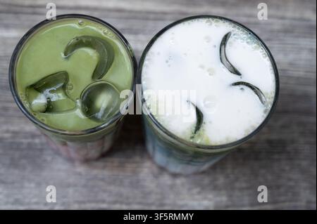 Vista aerea di due bevande ghiacciate al matcha in bicchieri di vetro trasparenti con fette di cetriolo e ghiaccio su un tavolo di legno consumato, che mostra una bevanda schiumosa verde pallido Foto Stock