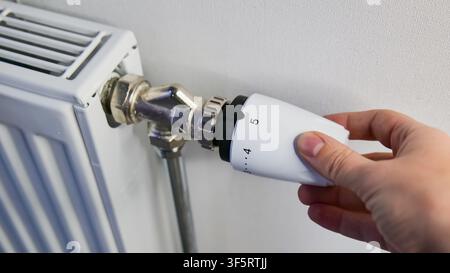 Mano che regola la temperatura su un radiatore montato a parete Foto Stock