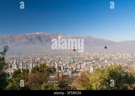 Cabine del teleferico di Santiago che scivolano sopra lo skyline urbano esteso con l'imponente catena delle Ande sullo sfondo a Santiago, Cile Foto Stock