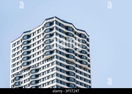 Edificio residenziale di lusso moderno con architettura elegante curva, finestre di vetro e balconi contro un cielo blu. Immobiliare urbana contemporanea Foto Stock