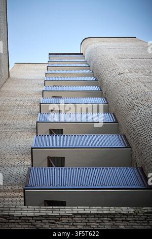Scatto a bassa angolazione di un edificio residenziale brutalista in mattoni con balconi impilati in cemento, ringhiere metalliche, texture curva della facciata sotto un blu chiaro Foto Stock